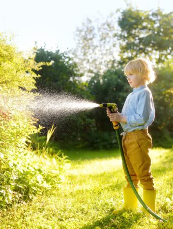 little boy watering a garden featured image for reduce water usage in the garden