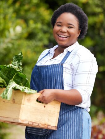 low maintenance plants picture of smiling black woman holding a box of leafy greens in a garden