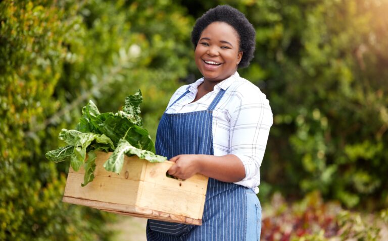 low maintenance plants picture of smiling black woman holding a box of leafy greens in a garden