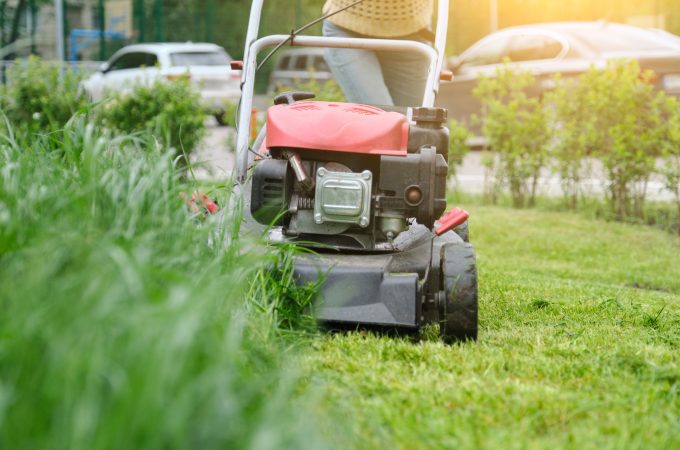 Lawn mower cutting green grass, gardener with lawnmower working, city courtyard of an apartment building