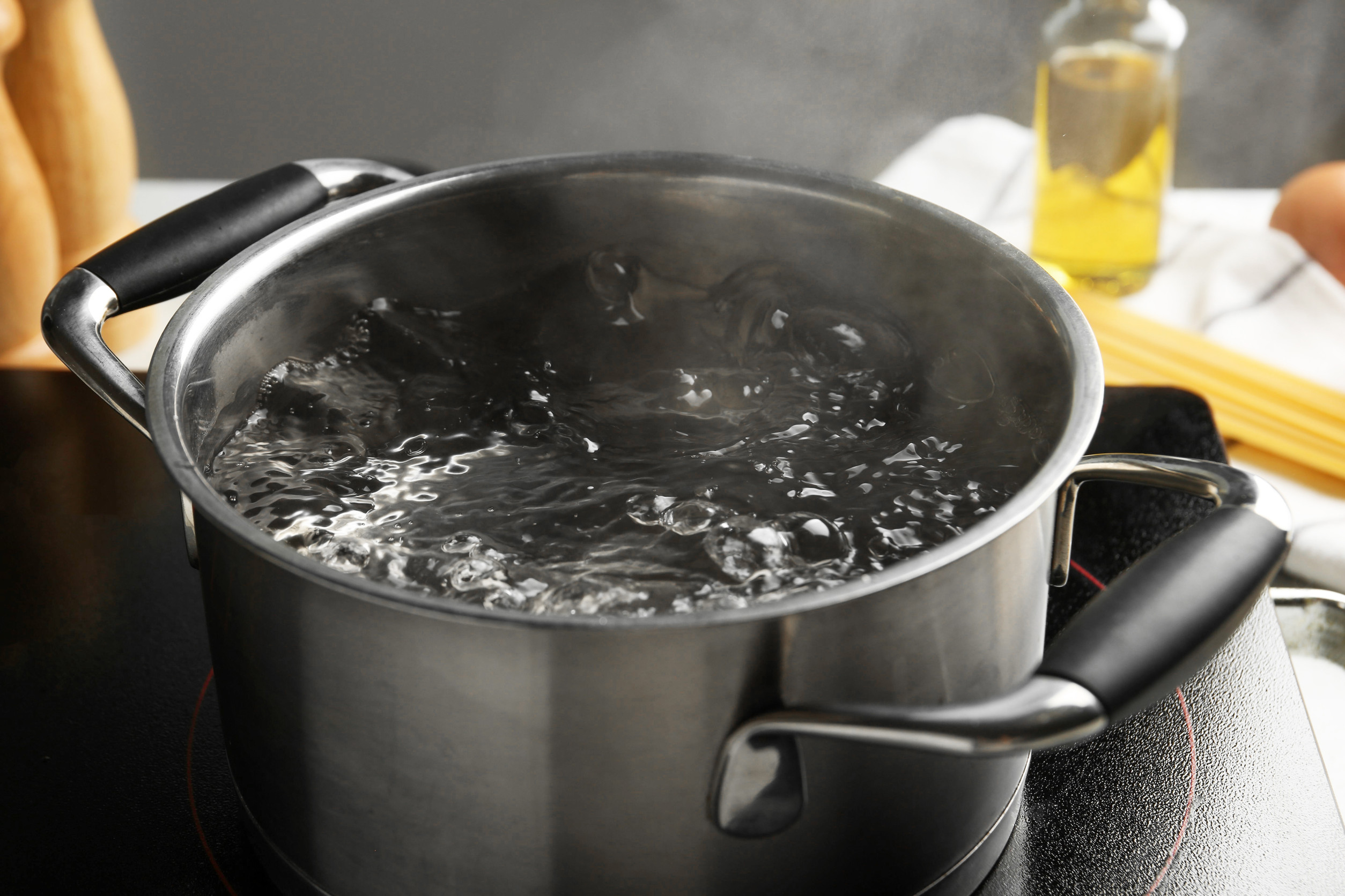 Cooking pot with boiling water and stove on white table against grey background, closeup